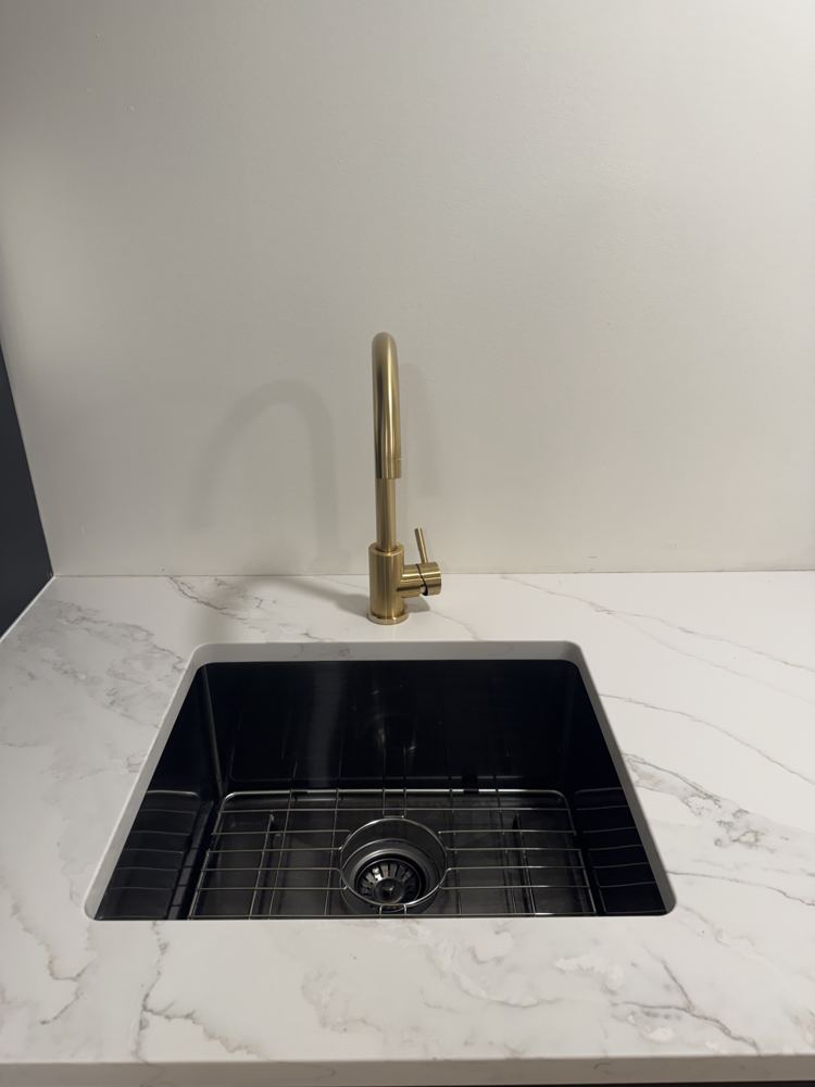 Black kitchen sink with gold faucet and white countertop